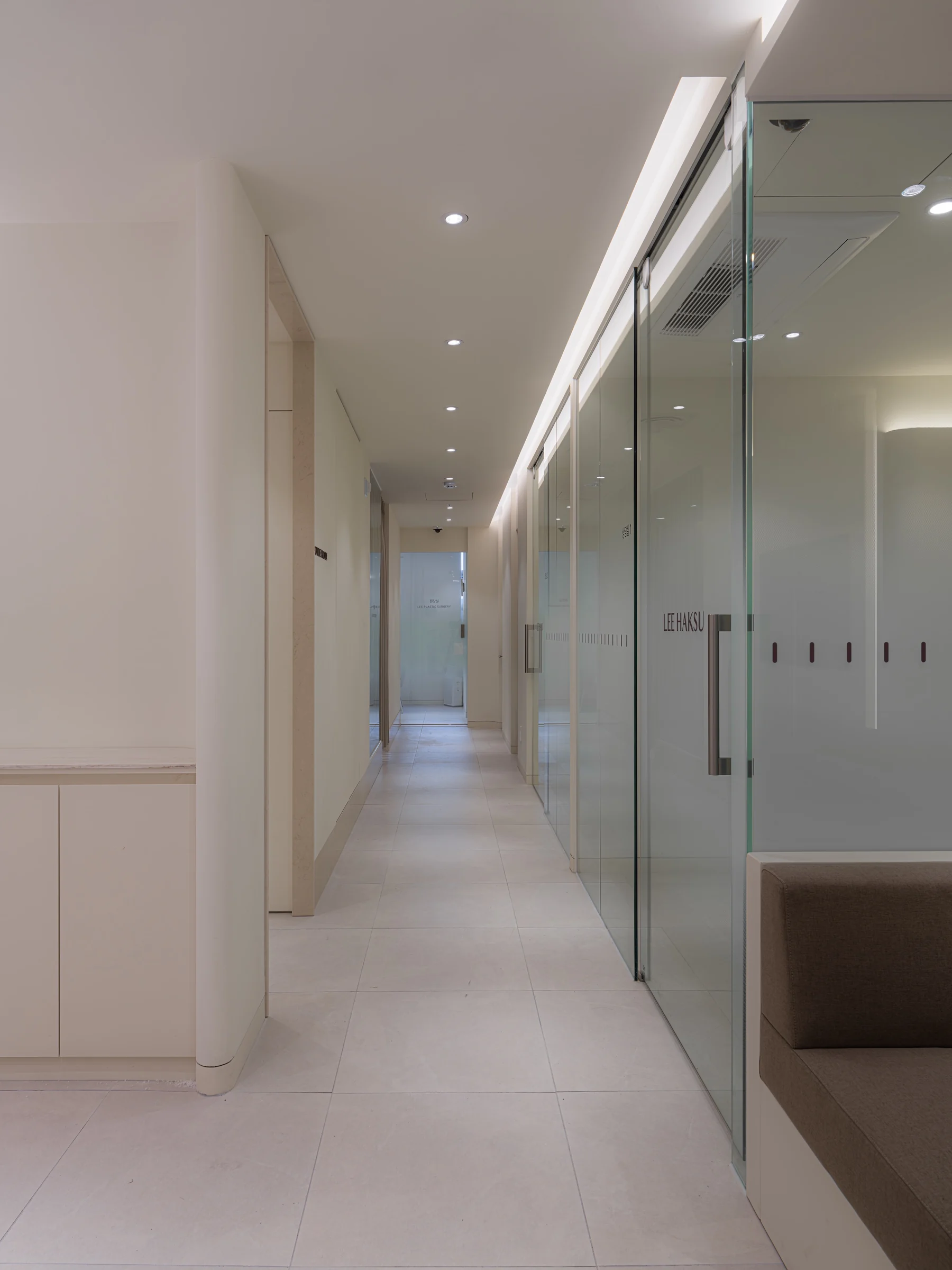 Corridor lined with private consultation rooms behind frosted glass doors marked LEE HAKSU