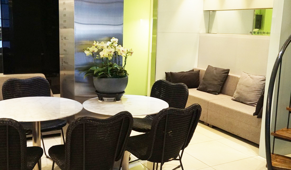 Consultation and waiting lounge with round tables, black chairs, a beige sofa, and a green art wall